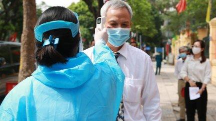 Una sanitaria vietnamita toma la temperatura a un ciudadano.