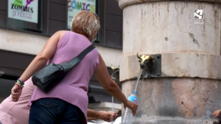 Una señora se refresca en la fuente de la plaza del Torico en Teruel.