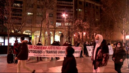 Varios transeúntes pasan por delante de los trabajadores del tranvía y de los autobuses urbanos concentrados en la Plaza Aragón de Zaragoza.