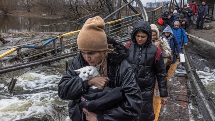 Una mujer con su gato cruza un puente destruido mientras los residentes huyen desde el frente de la ciudad de Irpín, en Kiev. / EFE