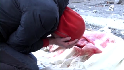 Una mujer ucraniana llora junto a un cadáver cubierto.