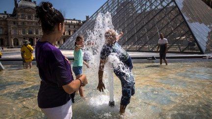 Un grupo de personas se refresca en una frente al Museo del Louvre, en París. / EFE