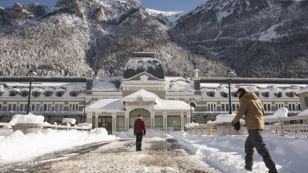 Varias personas pasan delante del edificio de la antigua estación de tren de Canfranc, cubierta por la nieve acumulada. / EFE.