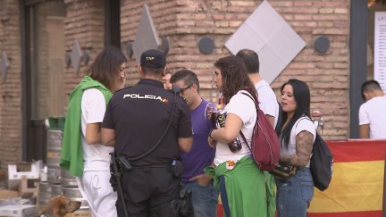 Un agente de Policía Nacional junto a un grupo de peñistas en la plaza del Pilar. / Aragón TV