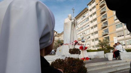 Un grupo de personas reza frente a la estatua del papa Juan Pablo II, delante del hospital en el que está ingresado el papa Francisco. / EFE