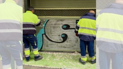 Dos operarios municipales limpian grafitis en un comercio de Huesca. / Ayuntamiento de Huesca