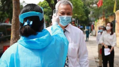 Una sanitaria vietnamita toma la temperatura a un ciudadano.