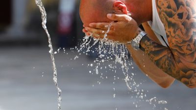 Un hombre se refresca con agua en una fuente (EFE).
