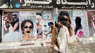Dos hombres pasan delante de un salón de belleza de Kabul en cuyo escaparate aparecen varios rostros femeninos que han sido desfigurados. (EP)