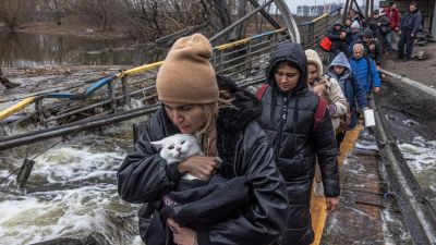 Una mujer con su gato cruza un puente destruido mientras los residentes huyen desde el frente de la ciudad de Irpín, en Kiev. / EFE