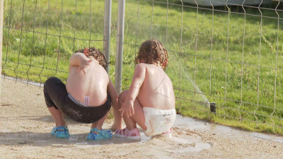 Dos niños tratando de refrescarse con ayuda de un aspersor.