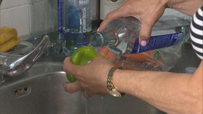 Una mujer lava la verdura con agua embotellada.