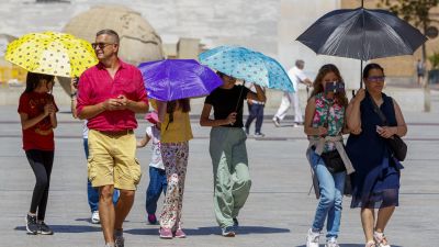 Un grupo de turistas pasea protegiéndose del sol por la plaza del Pilar. / EFE
