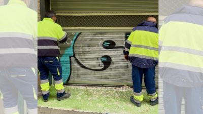 Dos operarios municipales limpian grafitis en un comercio de Huesca. / Ayuntamiento de Huesca