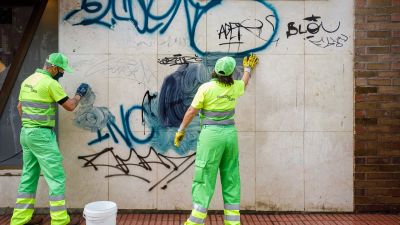 Trabajadores de limpieza eliminan grafitis sobre una pared.